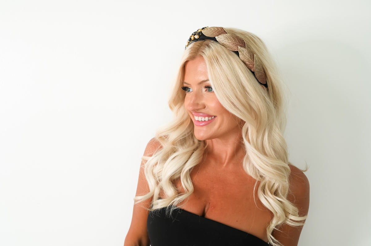 A smiling blonde woman with wavy hair wearing a brown braided headband with small gold decorative accents, photographed against a plain white background.